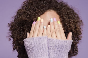 kvinna som håller händerna framför ansiktet med färgglada naglar